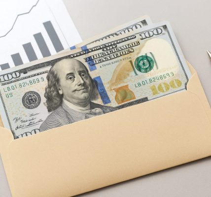 A close-up of an envelope containing cash and a pen, with a graph background