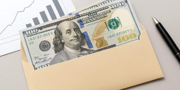 A close-up of an envelope containing cash and a pen, with a graph background